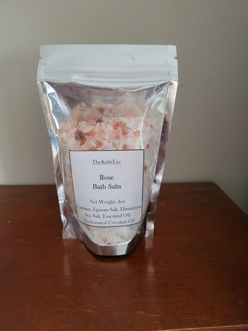 Puede incluir: Una bolsa de cierre herm&eacute;tico plateada llena de sales de ba&ntilde;o rosas del Himalaya. La etiqueta dice "The Katts Eye Rose Bath Salts Net Weight: 4oz Contains: Epsom Salt, Himalayan Sea Salt, Essential Oil, Fractionated Coconut Oil."