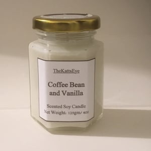Peut inclure: Une bougie en verre dans un pot avec un couvercle doré. L'étiquette indique "TheKattsEye Coffee Bean and Vanilla Scented Soy Candle Net Weight: 125gm/ 4oz"