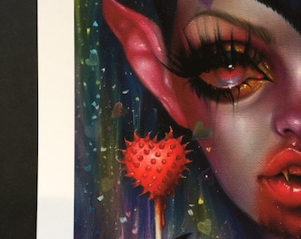 May include: A close-up of a fantasy art print featuring a character with red skin, long black nails, and a heart-shaped lollipop. The character has long eyelashes, red lips, and a dark background with colorful hearts.