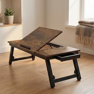 May include: A wooden laptop desk with a distressed brown finish and black legs. The desk has an adjustable top, a small drawer, and is designed to be used on a bed or sofa. The desk is approximately 24 inches long.