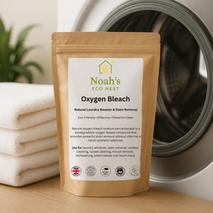 Może przedstawiać: Brązowa torebka z "Noah's Eco Nest Oxygen Bleach" stoi przed pralką i złożonymi białymi ręcznikami. Etykieta głosi "Natural Laundry Booster & Stain Removal" i wymienia zastosowania produktu.