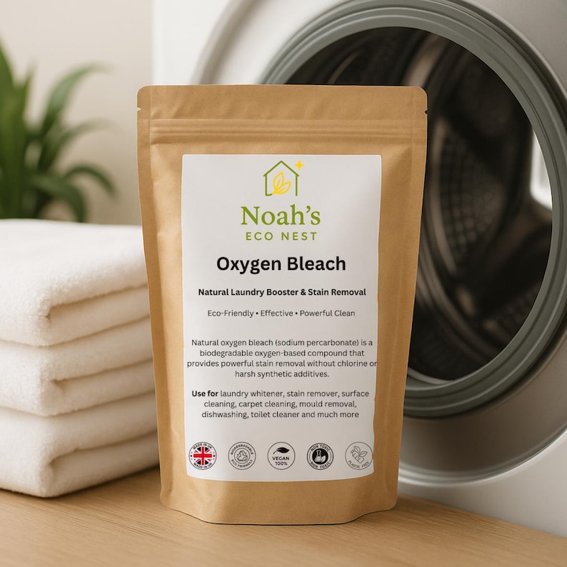 Może przedstawiać: Brązowa torebka z "Noah's Eco Nest Oxygen Bleach" stoi przed pralką i złożonymi białymi ręcznikami. Etykieta głosi "Natural Laundry Booster & Stain Removal" i wymienia zastosowania produktu.