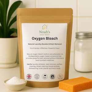 Może przedstawiać: Brązowa papierowa torebka z wybielaczem tlenowym Noah's Eco Nest, naturalnym wzmacniaczem prania i odplamiaczem. Etykieta głosi "Natural Laundry Booster & Stain Removal". Obok mała miska z białym proszkiem i pomarańczowa gąbka.