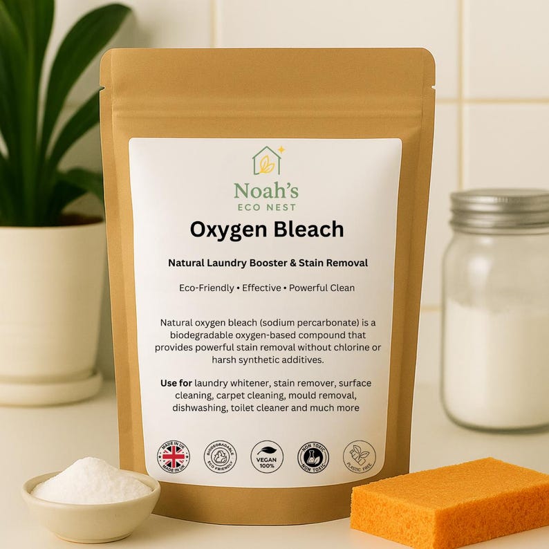 Może przedstawiać: Brązowa papierowa torebka z wybielaczem tlenowym Noah's Eco Nest, naturalnym wzmacniaczem prania i odplamiaczem. Etykieta głosi "Natural Laundry Booster & Stain Removal". Obok mała miska z białym proszkiem i pomarańczowa gąbka.
