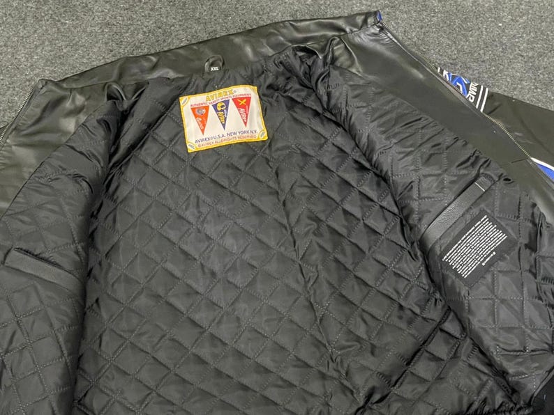 以下が含まれることがあります： 黒い革のジャケット、キルティング加工された黒い裏地付き。 ジャケットの内側にはテキスト入りのラベルと、赤、黄、青の旗のパッチが付いています。 ジャケットは開いており、内部の詳細が明らかになっています。