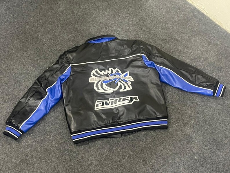 以下が含まれることがあります： 黒い革のジャケットで、袖と襟に青いアクセントがあります。背面には白と青のグラフィックと「Avirex」の文字があります。ジャケットは、青と白のストライプが入ったリブ編みの裾と袖口が付いています。