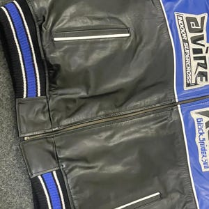 以下が含まれることがあります： 白のアクセントが付いた黒と青のレザージャケット。ジッパー開閉、2つのフロントポケット、青と白のストライプのリブ編みカフスが特徴です。ジャケットには「AVIRE INDOOR SUPERCROSS」と「Black Spider 500」の文字が入っています。