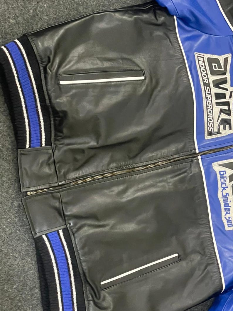 以下が含まれることがあります： 白のアクセントが付いた黒と青のレザージャケット。ジッパー開閉、2つのフロントポケット、青と白のストライプのリブ編みカフスが特徴です。ジャケットには「AVIRE INDOOR SUPERCROSS」と「Black Spider 500」の文字が入っています。