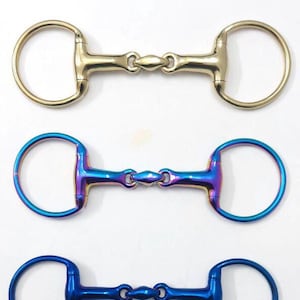 Op de afbeelding: Drie paardenbitten in goud, iriserend blauw en blauw. Elke bit heeft aan weerszijden een cirkelvormige ring die is verbonden door een centraal gewricht. De gouden bit staat bovenaan, gevolgd door een iriserende blauwe bit en een blauwe bit onderaan.