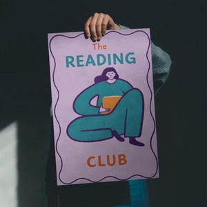 May include: A poster with the text "The Reading Club" in teal and orange, featuring an illustration of a person in teal clothing holding a book. The poster has a purple border and is held up by a hand.