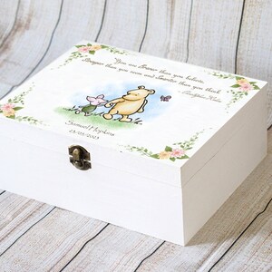 May include: White wooden keepsake box with a hinged lid and metal clasp. The lid features a Winnie the Pooh illustration with Piglet, a butterfly, and a quote. Floral and leaf accents frame the top. The box is personalized with a name and date.