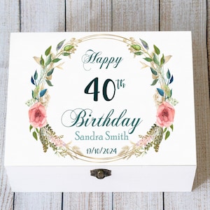 May include: White wooden box featuring a floral wreath design and the text "Happy 40th Birthday Sandra Smith 19/10/2024". The wreath includes pink roses, green leaves, and gold accents. The box has a metal clasp.