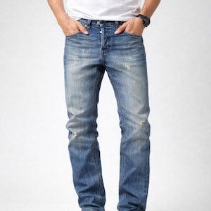 Può includere: Jeans blu sbiaditi con dettagli strappati, abbinati a una t-shirt bianca e scarpe da ginnastica bianche. I jeans hanno un classico design a cinque tasche e una chiusura con bottoni. L'aspetto è casual e moderno.