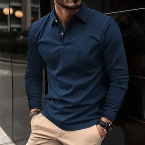Puede incluir: Un polo de manga larga azul marino con cuello clásico y tapeta abotonada. La camisa tiene un bolsillo en el pecho y está hecha de una tela lisa de color liso. El modelo lleva pantalones color caqui y un reloj negro.