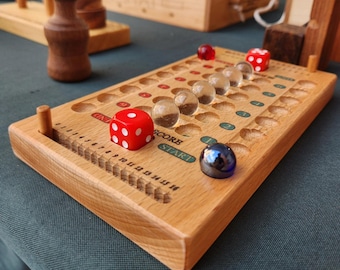 May include: A wooden board game with a series of holes and a scoring track. The game includes red dice and clear glass marbles. The board is made of light-colored wood and has the words "SCORE" and "START" printed on it.