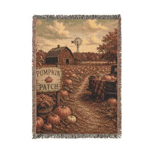 May include: A woven throw blanket featuring a rustic autumn scene with a pumpkin patch, a wooden sign reading PUMPKIN PATCH, a red barn, a windmill, and a vintage truck. The design uses warm earth tones including orange, brown, and tan colors.