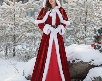Könnte beinhalten: Ein roter Samt-Kapuzenmantel und ein passendes Kleid mit weißem Kunstfellbesatz. Der Umhang hat goldene Stickereien und einen schwarzen Gürtel. Das Outfit wird mit weißen Handschuhen getragen.