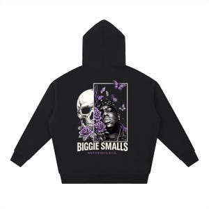 May include: Black hoodie featuring a graphic of a skull and a portrait of Biggie Smalls, with purple roses and butterflies. The text "BIGGIE SMALLS NOTORIOUS B.I.G." is printed below the portrait. The hoodie has a hood and long sleeves.