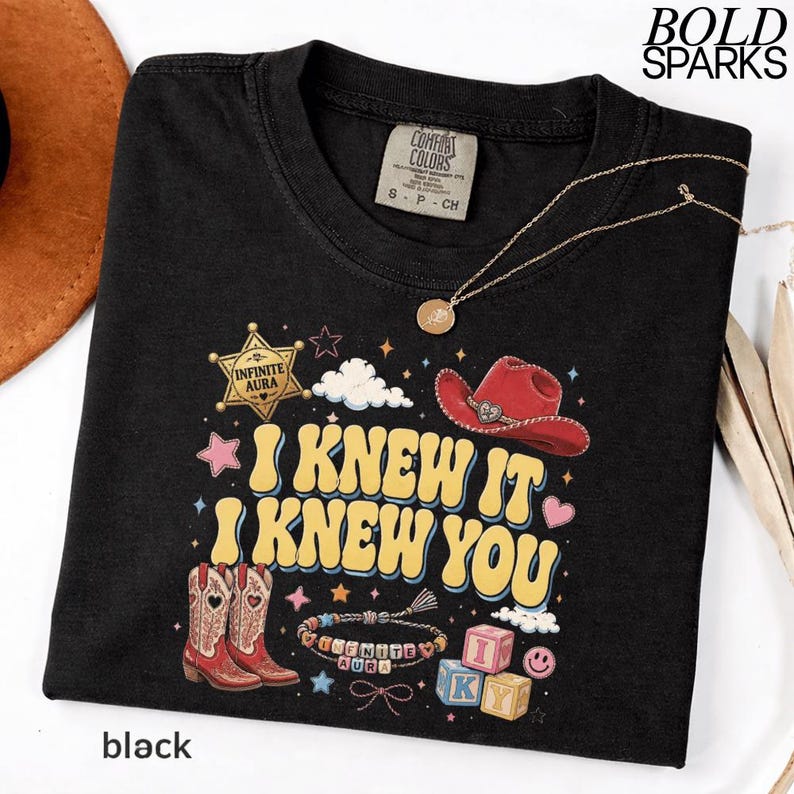 Może przedstawiać: Czarny t-shirt z nadrukiem graficznym z ż&oacute;łtym napisem I KNEW IT I KNEW YOU. Wz&oacute;r zawiera czerwony kowbojski kapelusz, parę kowbojek, gwiazdę szeryfa, bransoletkę z koralik&oacute;w, klocki z literami oraz małe gwiazdki i chmurki na czarnym tle.
