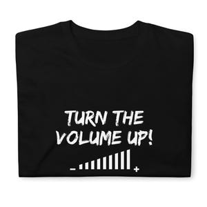 May include: Black t-shirt featuring the white text "TURN THE VOLUME UP!" and a volume control graphic. The t-shirt is folded, showing the front of the garment.