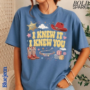 Może przedstawiać: Niebieski t-shirt z nadrukiem graficznym z tekstem I KNEW IT I KNEW YOU. Wz&oacute;r zawiera ż&oacute;łtą gwiazdę szeryfa, czerwony kowbojski kapelusz, parę kowbojek, bransoletkę z koralik&oacute;w z napisem INFINITE AURA oraz klocki z literami.
