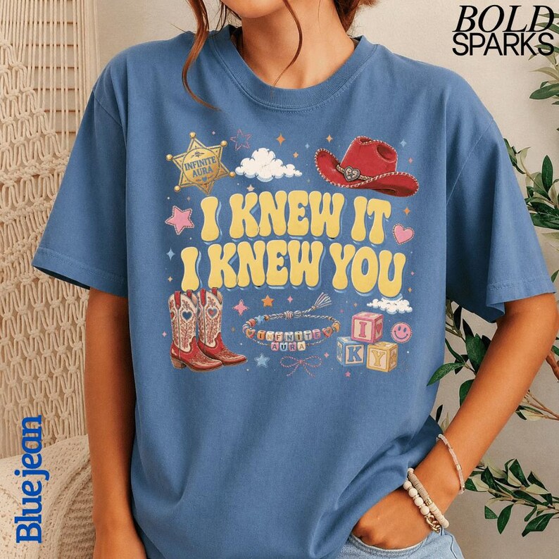 Może przedstawiać: Niebieski t-shirt z nadrukiem graficznym z tekstem I KNEW IT I KNEW YOU. Wz&oacute;r zawiera ż&oacute;łtą gwiazdę szeryfa, czerwony kowbojski kapelusz, parę kowbojek, bransoletkę z koralik&oacute;w z napisem INFINITE AURA oraz klocki z literami.