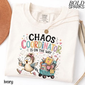 Può includere: Una t-shirt color avorio con la grafica di un uccellino frenetico che tiene in mano una tazza di caffè e trascina un carretto pieno di materiale scolastico, libri e una cartellina con la scritta IEP. Il testo recita CHAOS COORDINATOR IS ON THE WAY e HOLD ON, WE'RE DOING OUR BEST.
