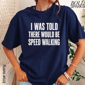 May include: A navy blue short-sleeved t-shirt featuring the white distressed text I WAS TOLD THERE WOULD BE SPEED WALKING printed on the center of the chest. The shirt has a crew neckline and a standard fit, showcasing a casual design.