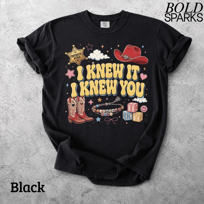 Może przedstawiać: Czarny t-shirt z kr&oacute;tkim rękawem z nadrukiem graficznym z tekstem I KNEW IT I KNEW YOU. Wz&oacute;r zawiera czerwony kowbojski kapelusz, gwiazdę szeryfa z napisem INFINITE AURA, parę czerwonych kowbojek, bransoletkę z koralik&oacute;w oraz klocki z literami.