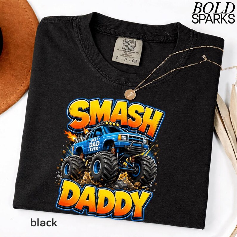 May include: Black t-shirt with a graphic of a blue monster truck with the words "SMASH DADDY" in yellow and orange. The text "BEST DAD EVER" is on the truck. The shirt has a Comfort Colors tag and a gold necklace.