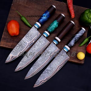May include: Four Damascus steel chef knives with patterned blades and colorful handles. The handles are dark brown, blue, green, and black. The blades have a unique pattern. The text "DAMASCUS LAB" is visible on the wooden cutting board.