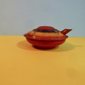 Puede incluir: Una tetera de metal roja, amarilla y azul con un pico y una tapa. La tetera est&aacute; ligeramente desgastada y tiene un acabado moteado.