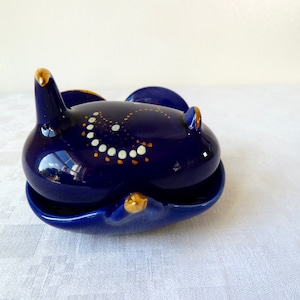 Puede incluir: Un plato de cerámica azul con un borde dorado y detalles pintados en blanco y oro. El plato tiene forma de pájaro y tiene una tapa.