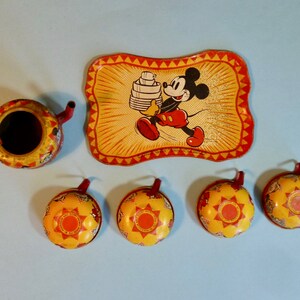 May include: A vintage Mickey Mouse tea set made of tin. The set includes a teapot, four cups, and a tray with a picture of Mickey Mouse carrying a stack of dishes. The set is yellow, red, and black.