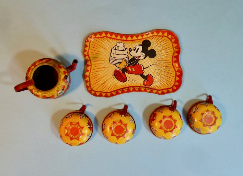 May include: A vintage Mickey Mouse tea set made of tin. The set includes a teapot, four cups, and a tray with a picture of Mickey Mouse carrying a stack of dishes. The set is yellow, red, and black.