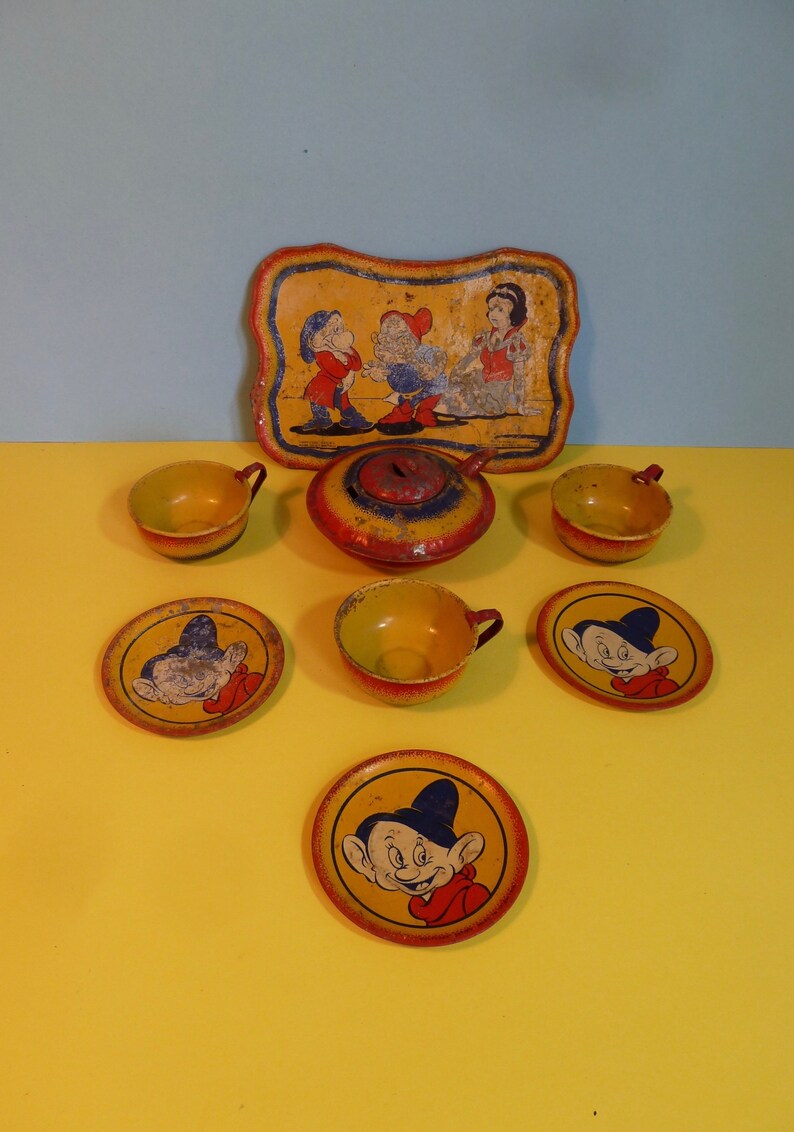 Puede incluir: Un juego de t&eacute; de hojalata vintage con Blancanieves y los Siete Enanitos. El juego incluye una tetera, cuatro tazas, cuatro platillos y una bandeja con una imagen de Blancanieves y dos enanos. El juego est&aacute; pintado en colores brillantes, incluyendo rojo, amarillo, azul y verde.