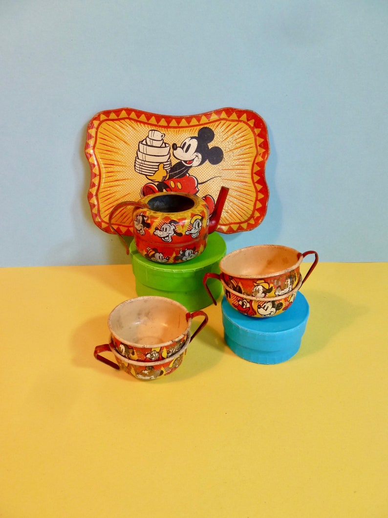 May include: A vintage Mickey Mouse tea set featuring a red and yellow teapot, three red and yellow cups, and a red and yellow tray with a Mickey Mouse image. The tray has the text "Mickey Mouse" on it.
