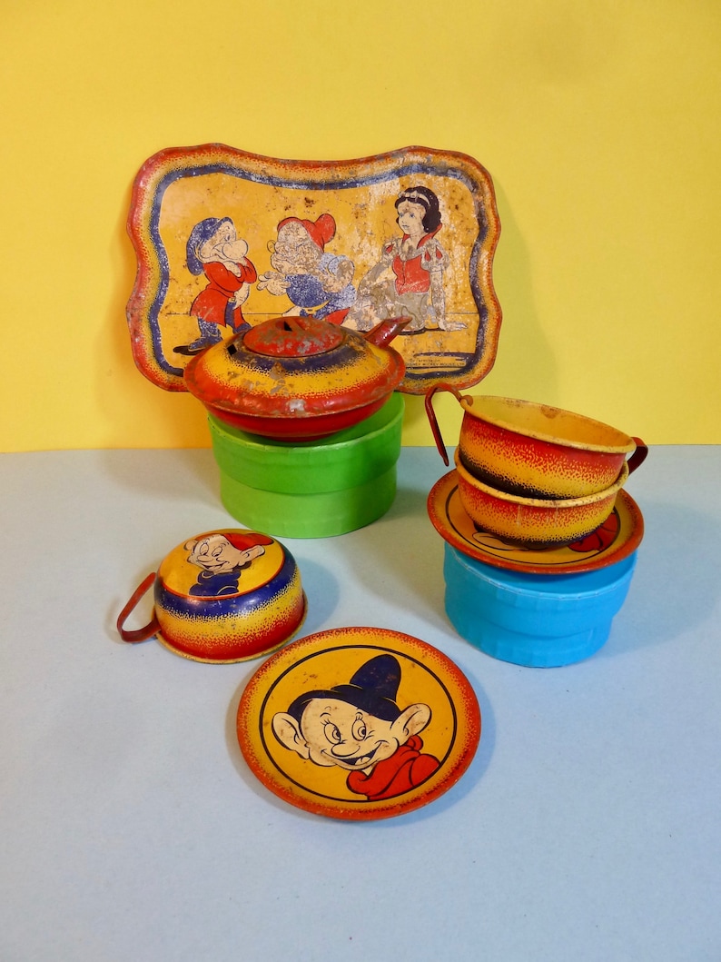 Puede incluir: Juego de t&eacute; de juguete de hojalata vintage con Blancanieves y los Siete Enanitos. El juego incluye una tetera, dos tazas, dos platillos y una bandeja. La tetera y las tazas est&aacute;n decoradas con im&aacute;genes de los enanitos, mientras que la bandeja presenta a Blancanieves y dos enanitos. El juego est&aacute; en buen estado con algunas se&ntilde;ales de desgaste.