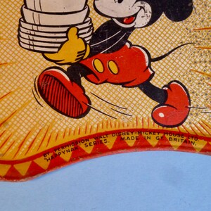 May include: A yellow and red vintage tin plate featuring Mickey Mouse carrying a stack of plates. The text "By Permission Walt Disney-Mickey Mouse Ltd. Happynak Series. Made in Gt Britain." is printed on the bottom of the plate.