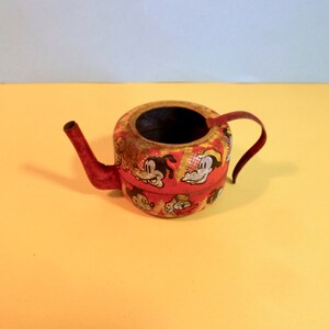May include: A red and yellow metal watering can with a cartoon character design. The can has a spout and a handle.