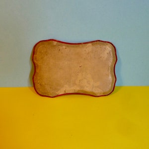 May include: A rectangular tray with a red rim and a light brown, slightly textured surface. The tray is empty.