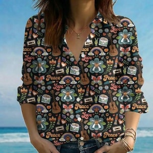May include: Black button-down shirt with a colorful, all-over print featuring flowers, guitars, rainbows, peace signs, and the words "Peace" and "Love". The shirt has long sleeves and a V-neck collar.