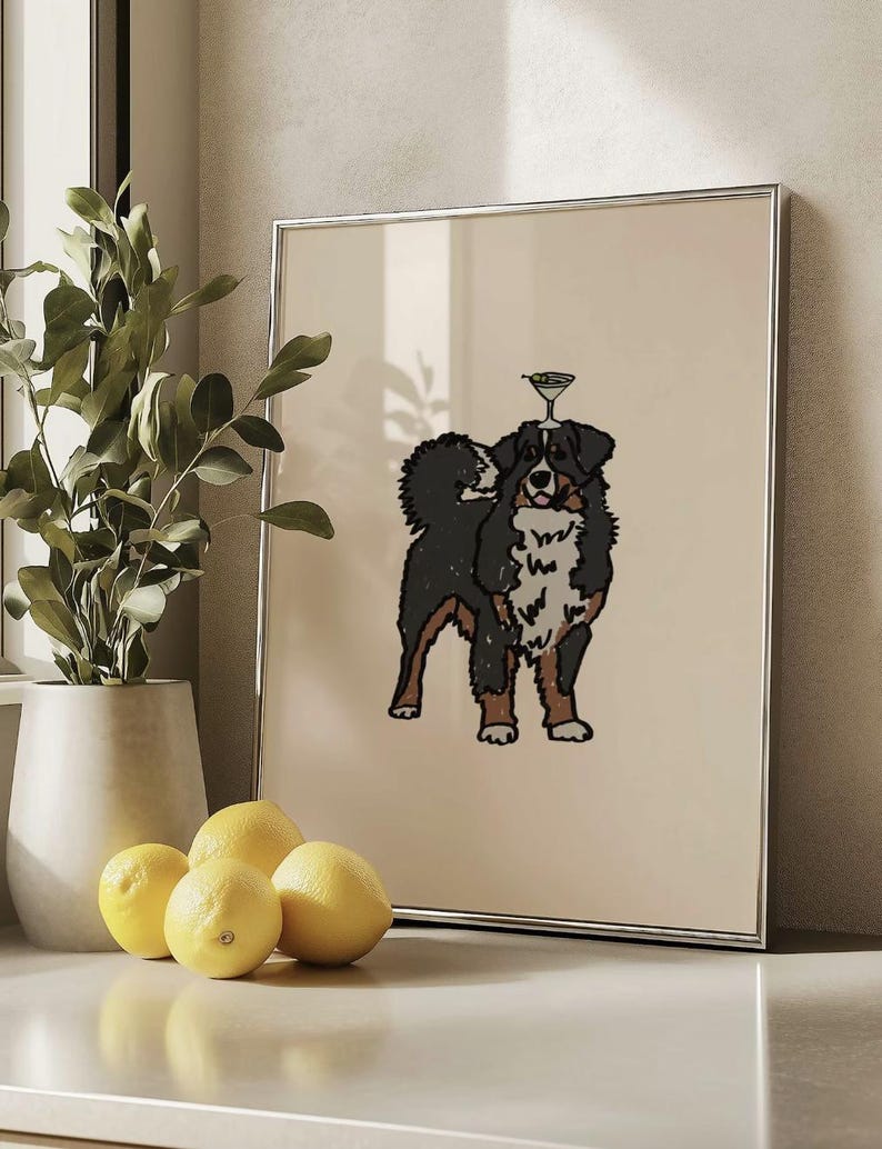 May include: A framed wall art print featuring a stylized illustration of a Bernese Mountain Dog with a martini glass balanced on its head. The dog has black, white, and brown fur, and the background of the print is a solid light beige color.