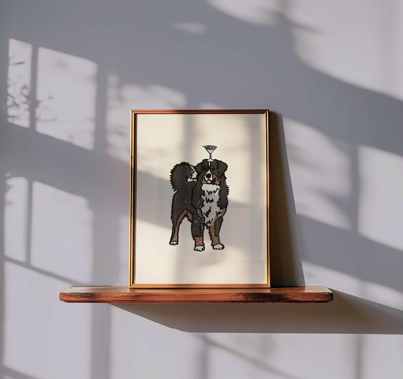 May include: A framed art print featuring a black, brown, and white Bernese Mountain Dog standing with a martini glass balanced on its head. The illustration is centered on a cream-colored background within a thin, metallic gold-toned frame.