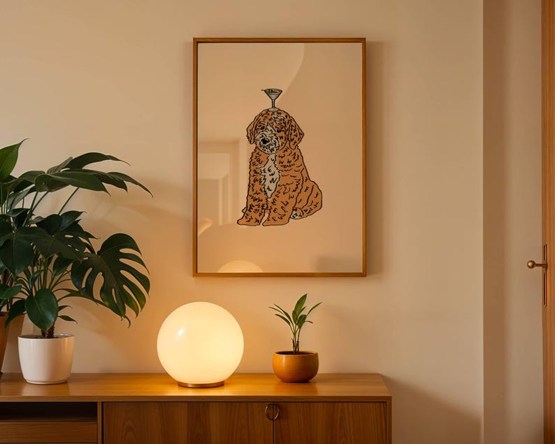 May include: A framed wall art print featuring a brown, curly-haired dog sitting down with a small martini glass balanced on its head. The illustration uses bold black outlines against a solid, light beige background within a wooden frame.