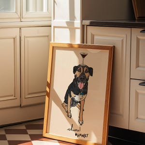 May include: A framed illustration of a black and tan dog with its tongue out, balancing a martini glass on its head. The artwork features a light beige background with the handwritten text "cheers!" and the name "HANLEY" printed below the dog.