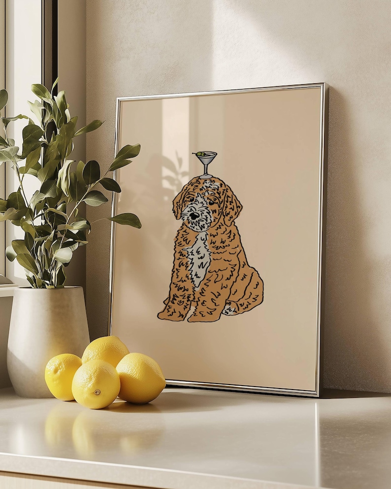 May include: A framed wall art print featuring a line-art illustration of a golden-brown curly-haired dog sitting down with a martini glass balanced on its head, set against a solid light beige background within a thin silver frame.
