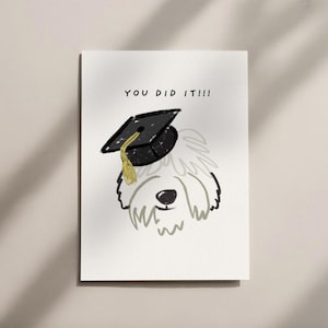 Puede incluir: Tarjeta de felicitación de graduación con un dibujo de un perro con un birrete negro con borla dorada. Las palabras "YOU DID IT!!!" están escritas encima de la cabeza del perro.