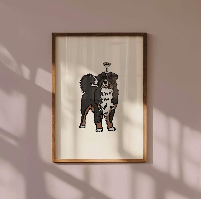 May include: A framed wall art print featuring a stylized illustration of a Bernese Mountain Dog with black, white, and brown fur. The dog is standing and has a small, outlined martini glass balanced on top of its head against a cream background.