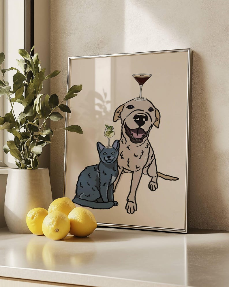 May include: A framed wall art print featuring a line-art illustration of a smiling light-coloured dog and a grey cat sitting together. The dog has a martini glass balanced on its head, and the cat has a smaller cocktail glass on its head.